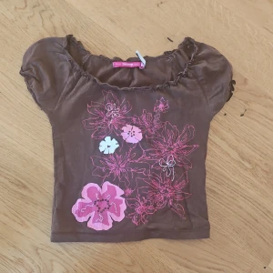 Brun topp med blommönster - Söt vintage topp från indiska med korta puffärmar och ett stort blommönster i rosa och vitt framtill. 