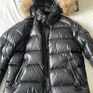 Svart dunjacka från Moncler - Säljer en snygg svart pufferjacka från Moncler i mycket bra skick. Jackan har en fluffig pälsfodrad huva och dragkedja framtill. Perfekt för kalla vinterdagar! Storleken är inte angiven, men den ser ut att vara normal i passformen storlek L. Hör av dig vid intresse! 🖤