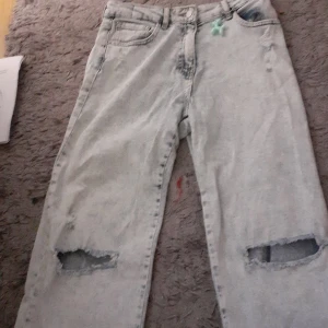 Ljusa jeans med slitningar - Säljer ett par ljusa jeans från I Love Girlswear. De har coola slitningar på knäna och en avslappnad passform. Perfekta för en casual look! De är i bra skick och har en justerbar midja för bästa passform.