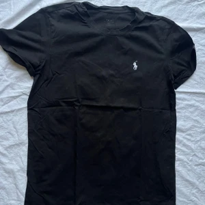 Svart t-shirt från Ralph Lauren - Säljer en klassisk svart t-shirt från Ralph Lauren i herrstorlek M. Den har en broderad logga på bröstet och är gjord i mjuk bomull. Perfekt för en stilren och avslappnad look. Passar till både vardag och fest!