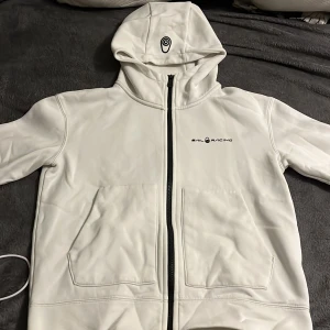 Vit hoodie från Sail Racing - Säljer en snygg vit hoodie från Sail Racing i mycket bra skick. Den har en dragkedja framtill och en praktisk huva. Perfekt för både vår och höst. Den är gjord i ett mjukt och bekvämt material, perfekt för vardagsbruk. Passar xs och s