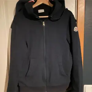 Säljer en snygg marinblå hoodie från Moncler i storlek M. Den har en dragkedja framtill och en praktisk huva. Perfekt för höst och vår, med en stilren design och Moncler-logga på ärmen. Passar både till vardags och lite mer avslappnade tillfällen.