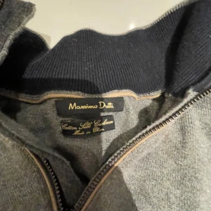 Grå tröja från Massimo Dutti - Säljer en stilren grå tröja från Massimo Dutti i bomull, silke och kashmir. Tröjan har en dragkedja vid halsen och är perfekt för både vardag och lite finare tillfällen. Den är mjuk och bekväm, perfekt för höst och vinter.