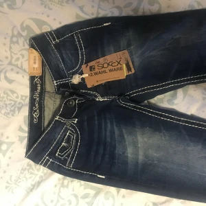 Mörkblå jeans från Soccx - Säljer ett par snygga mörkblå jeans från Soccx med coola slitningar och kontrastsömmar. De har en klassisk femficksdesign och en bekväm passform. Perfekta för en avslappnad vardagslook eller en utekväll. Märkeslappen sitter kvar, så de är i toppskick!