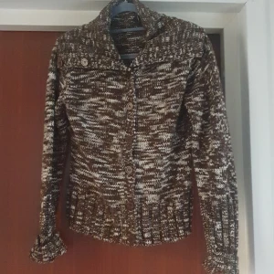 Brun och vit stickad kofta - Mysig brun och vit stickad kofta med knappar framtill. Perfekt för kyliga höst- och vinterdagar. Den har långa ärmar och en skön krage som håller dig varm. 