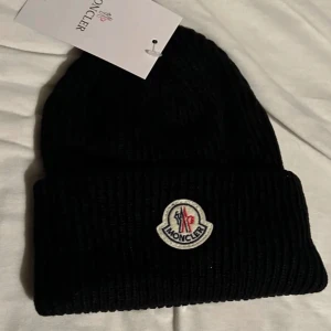 Svart mössa från Moncler - Snygg svart mössa från Moncler i nytt skick. Den är perfekt för kalla vinter dagar. Och den är enkel att matcha med olika outfits. Perfekt för vintern‼️ Och är jätte snygg ❄️😁 (jag kan diskutera priset) (original pris är 1600kr)