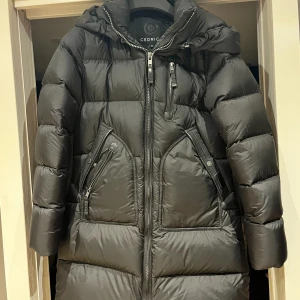 Svart dunjacka från Cedrico - Säljer en snygg och varm svart dunjacka från Cedrico i storlek S. Jackan har en praktisk huva och flera dragkedjefickor. Perfekt för kalla vinterdagar. Den är i mycket bra skick och redo för nya äventyr! 🖤