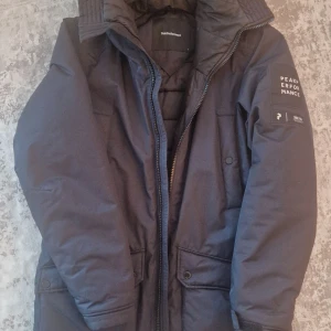 Svart vinterjacka från Peak Performance - Säljer en svart vinterjacka från Peak Performance i bra skick. Jackan har en dragkedja och knappar framtill, samt en hög krage för extra värme. Perfekt för kalla vinterdagar! 🖤