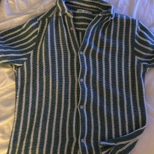 Randig sommar skjorta från Zara - Säljer en snygg randig skjorta från Zara i grönt och vitt. Skjortan har korta ärmar och knappar framtill. Perfekt för sommardagar eller en avslappnad vårlook. Materialet känns lätt och luftigt, vilket gör den bekväm att bära hela dagen.