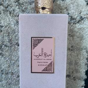 Säljer en lyxig parfym, Ameerat Al Arab Prive Rose från Asdaaf. Flaskan är elegant med en mjuk, ljusrosa yta och detaljer i guld. Doften är en blandning av ros och orientaliska toner, perfekt för speciella tillfällen. Kommer i en vacker förpackning som gör den till en fin present. Helt ny