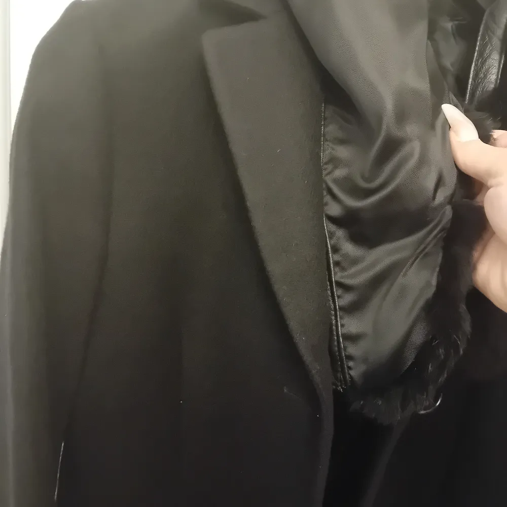 Säljer en elegant svart kappa med pälsdetaljer på kragen. Perfekt för kyliga höst- och vinterdagar. Den har en klassisk design med långa ärmar och knappar framtill. Passar både till vardags och festliga tillfällen.. Takit.