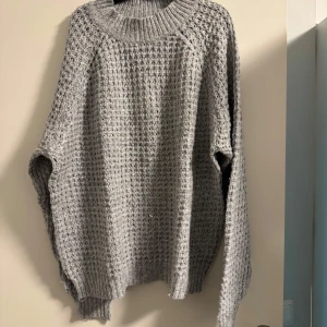 Grå stickad tröja från 157 - Mysig grå stickad tröja från 157 i storlek S. Perfekt för kyliga dagar med sin tjocka och varma design. Tröjan har en ribbad krage och långa ärmar, vilket gör den idealisk för både höst och vinter. Ett måste i garderoben för den som älskar komfort och stil!