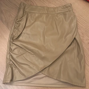 Beige omlottkjol - Säljer en superfin beige omlottkjol från Selma Omari x NA-KD. Kjolen har en snygg omlottdesign och är i ett skinnliknande material. Perfekt för både vardag och fest! 👜✨