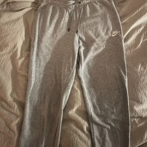 Grå mjukisbyxor från Nike - Säljer ett par grå mjukisbyxor från Nike i bra skick. De har en bekväm passform med dragsko i midjan och Nike-loggan på benet. Perfekta för en avslappnad dag hemma eller lätt träning. 🩶