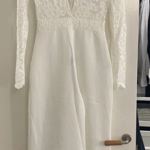 Vit byxdress med spetsdetaljer - Elegant vit byxdress med vackra spetsdetaljer på överdelen och långa ärmar. Perfekt för fest eller formella tillfällen. Klänningen har en v-ringad design och är i mycket bra skick.