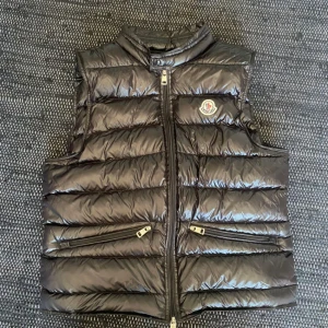 Svart dunväst från Moncler - Säljer en Moncler väst  i nyskick Västen har en glansig finish och dragkedja framtill. Perfekt till sommaren och våren den har även Moncler-loggan på bröstet den är i nyskick och den är äkta såklart kvitto finns!                       intresserad av byten också!