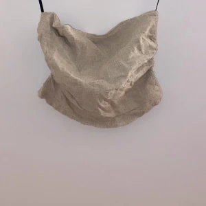 Beige glittrig linne - Snyggt beige linne med glittrig yta, perfekt för festliga tillfällen. Den är ärmlös och har en lös passform som ger en avslappnad men stilren look. Passar perfekt till både jeans och kjol för en chic outfit.