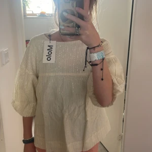 Vit glittrig blus från Molo - Säljer en superfin vit blus från Molo med glittriga detaljer. Blusen har trekvartsärmar och en lös passform, perfekt för både vardag och fest. Den är i nyskick och har knappar på baksidan. Storlek 134/140 men passar någon som är 153. 