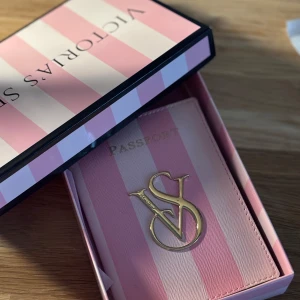 Victoria’s secret passfodral + låda gratis  - Säljer ett original supergulligt passfodral från Victoria's Secret i rosa och vita ränder. Med guldigt VS-emblem på framsidan och flera fack för kort på insidan. Perfekt för resan och att hålla ordning på passet med stil! Travel in style!! 🫶🏻🌸 