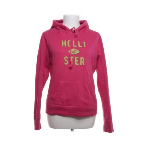 Rosa hoodie från Hollister - Säljer en snygg och bekväm rosa hoodie från Hollister. Perfekt för en avslappnad stil och passar bra till både jeans och mjukisbyxor. Hollister-loggan är tryckt i grön på framsidan. Perfekt för höst och vår! Jätte fint skick. Passar både S/M
