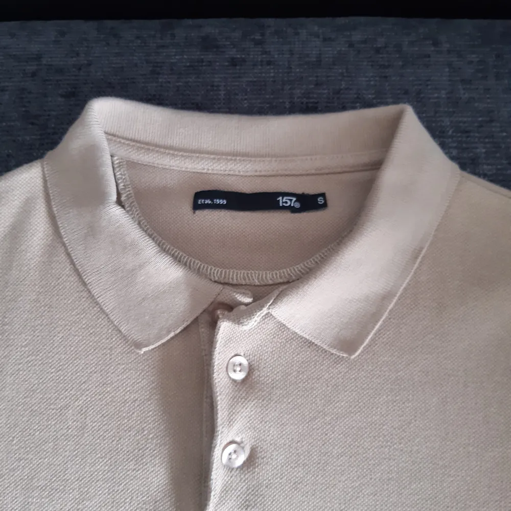 Säljer en stilren beige pikétröja från 157. Den har en klassisk krage och tre knappar framtill. Perfekt för en avslappnad men ändå snygg look. Passar bra till både vardag och lite finare tillfällen. Fint skick!!. T-shirts.