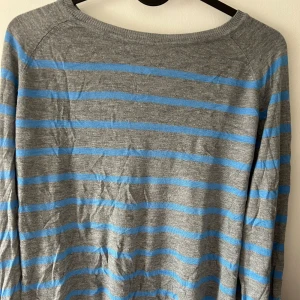 Grå och blå randig tröja - Säljer en snygg grå tröja med blå ränder. Den är perfekt för både vardag och lite kyligare dagar. Tröjan har långa ärmar och är superbekväm att ha på sig. Passar perfekt till jeans eller kjol! 