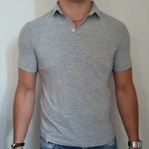 Grå randig pikétröja - Grå randig pikétröja av 85% bomull, 10% viskos och 5% elastan. Mjukt och luftigt material. Fint skick. Slim fit. 