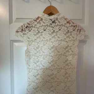 Vit spetsblus från Lindex - Säljer en superfin vit spetsblus från Lindex i storlek XS. Blusen har korta ärmar och är helt täckt i ett vackert blommigt spetsmönster. Perfekt för både fest och vardag!
