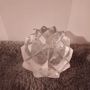 Säljer en superfin ljushållare i glas som ser ut som en kristallblomma. Den har en cool, geometrisk design med många facetter som reflekterar ljuset på ett magiskt sätt. Perfekt för att skapa mysig stämning hemma!