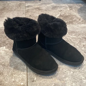 Svarta boots med pälsdetalj - Säljer ett par svarta ugg med fluffig pälsdetalj runt skaftet. De är perfekta för kalla dagar och har en robust sula för bra grepp. Pälsen går att tas in i skon om man hellre föredrar det. De är riktigt varma, perfekt för vintern. de är inte riktiga ugg, utan märket duffy men ser verkligen ut som ugg. Finns ett hål i pälsen på ena skon, men man märker inte det för pälsen är så tjock och fluffig. 