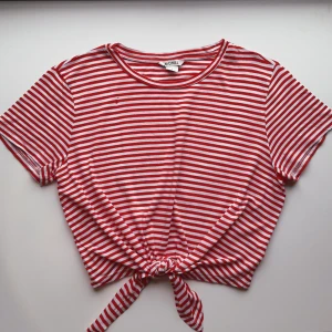 Randig tshirt med knytdetalj - Röd-vit randig tshirt med knytdetalj framtill som man själv knyter som man vill. Är i bra skick, förutom två små hål på framsidan och en liten fläck (se bilder). Skriv vid frågor! Lägg gärna prisförslag!