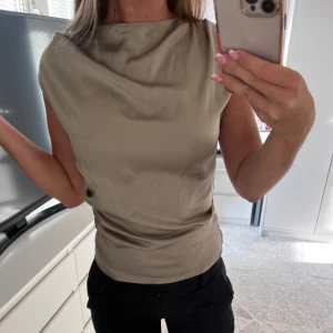 Grå grön blus - Säljer en elegant från grön blus i silkesmaterial från HM i storlek XS men  passar också som en S. Blusen har en fyrkantig halsringning och korta ärmar, vilket gör den perfekt för både vardag och fest. Blusen är i utmärkt skick pga ingen användning.