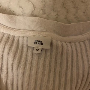 Vit ribbad kofta från River Island - Säljer en superfin vit ribbad kofta från River Island. Den har en v-ringad design med knappar framtill och långa ärmar. Perfekt för både vardag och fest! 🖤