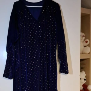 Mörkblå glittrig klänning - Snygg mörkblå klänning med glittrigt mönster. Den har långa ärmar och en v-ringad design som ger en elegant look. Perfekt för festliga tillfällen!