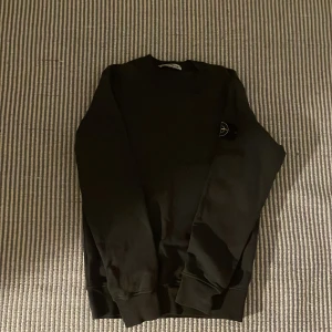 Svart sweatshirt från Stone Island - Säljer en snygg svart sweatshirt från Stone Island. Den har en klassisk design med rund hals och långa ärmar. Perfekt för både vardag och chill. Passar bra till jeans eller joggers! Använd endast ett fåtal gånger och i jätte bra skick. Säljer den då jag inte använder den tillräckligt mycket. NYPRIS-2300 kr, Pris kan diskuteras!