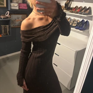 Brun offshoulder klänning - Snygg brun offshoulder klänning i ribbat material. Den har långa ärmar och en tight passform som framhäver figuren. Perfekt för höst och vinter, både till vardags och festliga tillfällen. Klänningen är stilren och enkel att matcha med olika accessoarer.