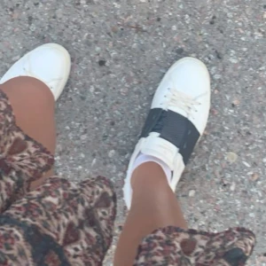 Valentino Garavani sneakers - Säljer ett par snygga Valentino Garavani sneakers i vitt skinn med en marinblå rem, i någon typ av krokodilmönster nästan? Dem är bra använda därav det låga priset men inget större fel på dem på fortfarande väldigt sköna och användbara. Skriv för mer frågor, det är en slitning inuti skon som jag kan skicka bild på ifall det behövs❤️