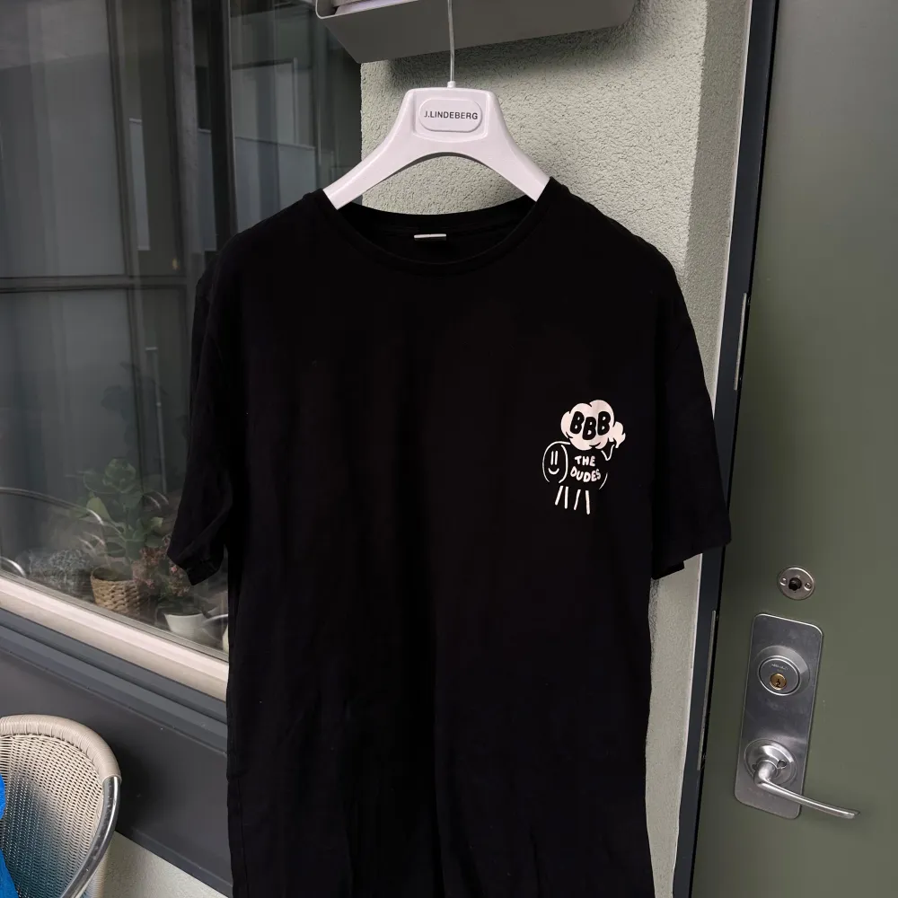 Säljer en svart t-shirt från The Dudes i storlek L. Den har ett coolt tryck med texten 'BBB The Dudes' på framsidan och ett större tryck med 'Bulleit Beer BBQ' på baksidan. Perfekt för en avslappnad stil eller BBQ-festen! T-shirten är i bra skick och gjord av mjuk bomull.. T-shirts.