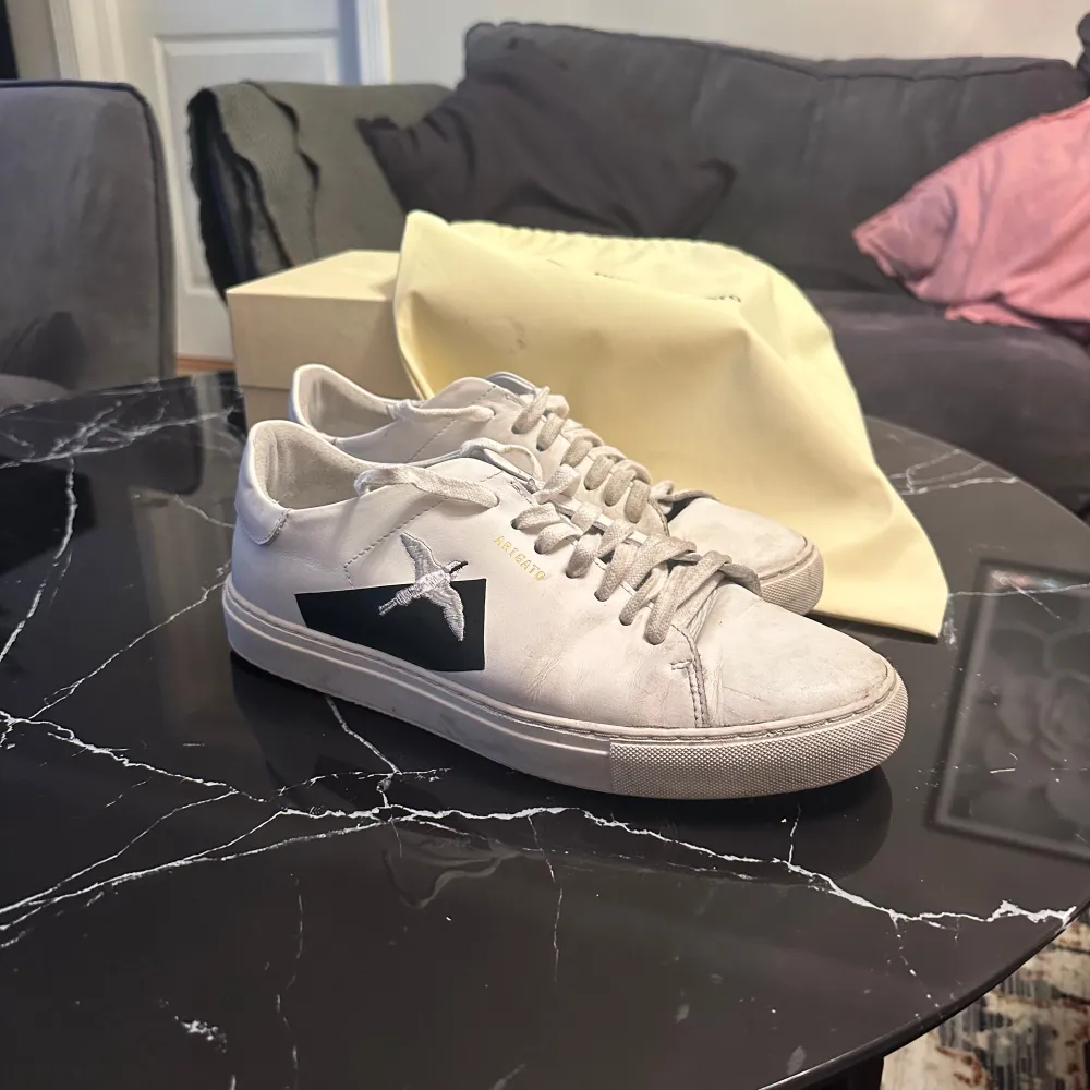 Säljer ett par stilrena vita sneakers från Axel Arigato. De har en snygg svart stjärndetalj på sidan och är i bra skick. Perfekta för både vardag och fest. Skorna har snörning och en bekväm passform.. Skor.