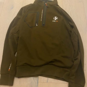 Olivgrön tröja från RLX - Säljer en olivgrön tröja från RLX i mycket bra skick. Den har en dragkedja vid halsen och en praktisk bröstficka med dragkedja. Perfekt för höst och vår, med långa ärmar och en bekväm passform. RLX-loggan syns både fram och bak. Passar både till vardags och träning.