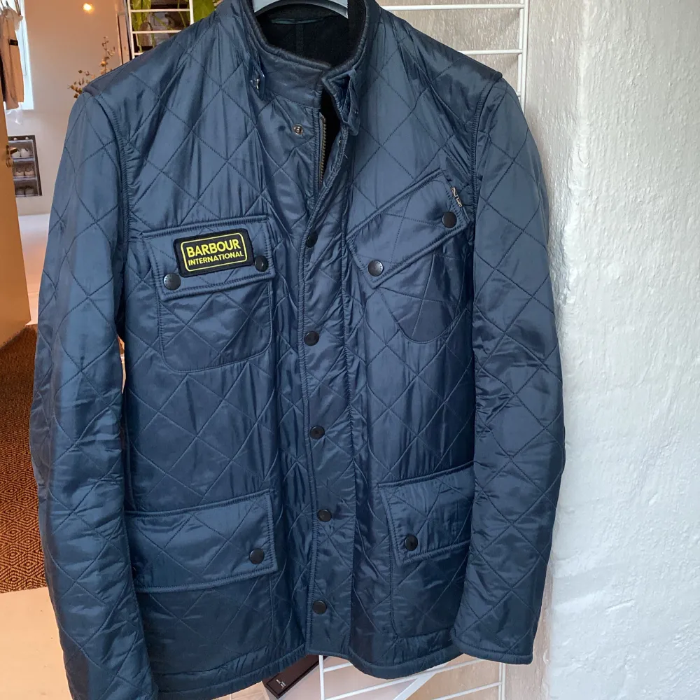 Säljer en snygg blå/grå quiltad jacka från Barbour. Skön fleece på insidan. Den har en dragkedja och knappar framtill, samt praktiska fickor. Jackan är perfekt för höst och vår. Jättesparsamt använd dock är själva draget på dragkedjan borta, se bild, men dragkedjan funkar utmärkt ändå samt kan jackan knäppas med knappar också. Strl M men sitter mer som en M-L.. Jackor.