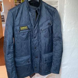 Säljer en snygg blå/grå quiltad jacka från Barbour. Skön fleece på insidan. Den har en dragkedja och knappar framtill, samt praktiska fickor. Jackan är perfekt för höst och vår. Jättesparsamt använd dock är själva draget på dragkedjan borta, se bild, men dragkedjan funkar utmärkt ändå samt kan jackan knäppas med knappar också. Strl M men sitter mer som en M-L.