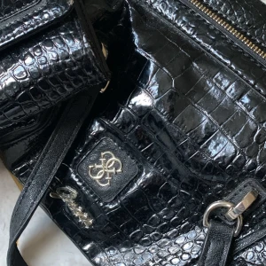 Svart axelväska guess väska och plånbok  - Snygg svart axelväska och matchande plånbok från Guess i krokodilmönstrat skinn. Väskan har en praktisk dragkedja och stilrena detaljer i silver. Perfekt för både vardag och fest!