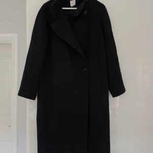 Svart kappa - Säljer en stilren svart kappa i mycket bra skick. Den har en klassisk design med långa ärmar och knappar framtill. Perfekt för höst och vinter, och passar både till vardags och fest. 