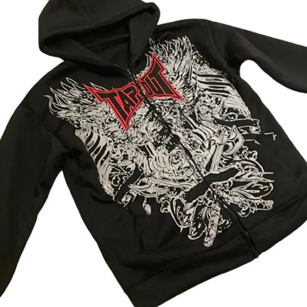 Säljer en svart hoodie från Tapout med ett coolt och detaljerat tryck i vitt och rött på framsidan. Den har en dragkedja och en skön huva, perfekt för en avslappnad stil. Passar bra till både vardag och träning. Hör av dig om du är intresserad!⚠️den är small men passar som s och m⚠️. Hoodies.