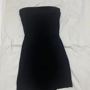 Svart axelbandslös klänning - Snygg svart axelbandslös klänning i kort modell. Perfekt för festliga tillfällen. Den har en tight passform som framhäver figuren. Enkelt och stilrent val för en kväll ute.