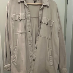 Beige overshirt från Divided - Säljer en beige overshirt från Divided i bra skick. Den har en avslappnad passform med knappar framtill och två stora bröstfickor. Perfekt för lager-på-lager under hösten eller våren. Passar både till vardags och lite mer uppklädda tillfällen.