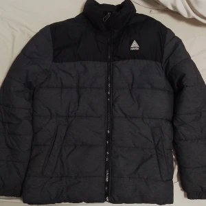 Svart och grå pufferjacka från H&M - Säljer en snygg svart och grå pufferjacka från H&M i herrstorlek M. Jackan har en dragkedja framtill och är perfekt för kyliga dagar. Den är i mycket bra skick och har en stilren design med ett litet märke på bröstet. Perfekt för höst och vinter!