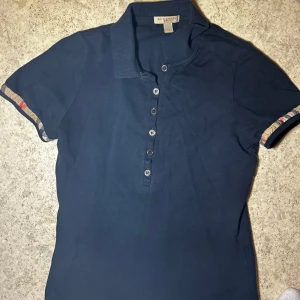 Mörkblå pikétröja från Burberry - Säljer en snygg mörkblå pikétröja från Burberry i storlek XS. Kondition 6/10 nypris ca 2500-3500 mitt pris 600 kr. Var snabb!