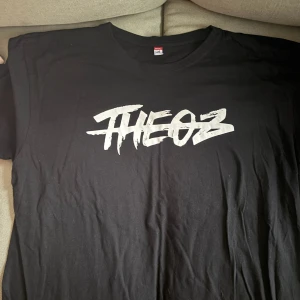 Svart och vit t-shirt med tryck - Två t-shirts med trycket 'THEOZ' i graffiti-stil. Den ena är svart med vitt tryck och den andra är vit med svart tryck. Perfekt för en casual look och passar till alla tillfällen. Båda är kortärmade och i bomullsmaterial.